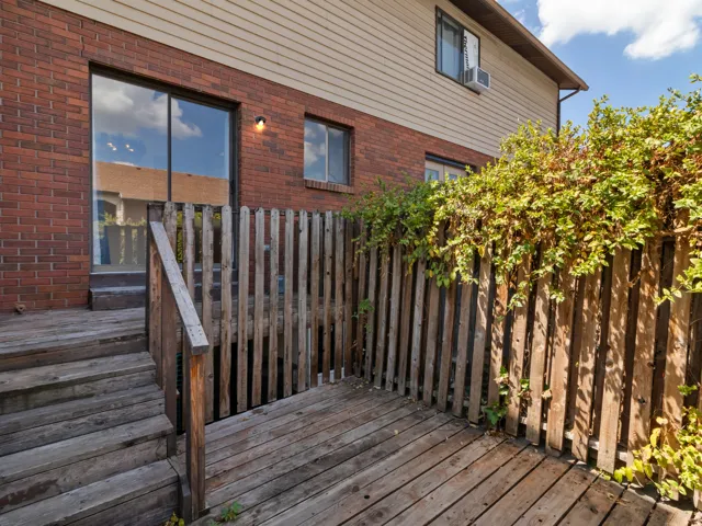Private wooden deck area featuring a sliding glass door entry, brick exterior, and wood privacy fence with established greenery