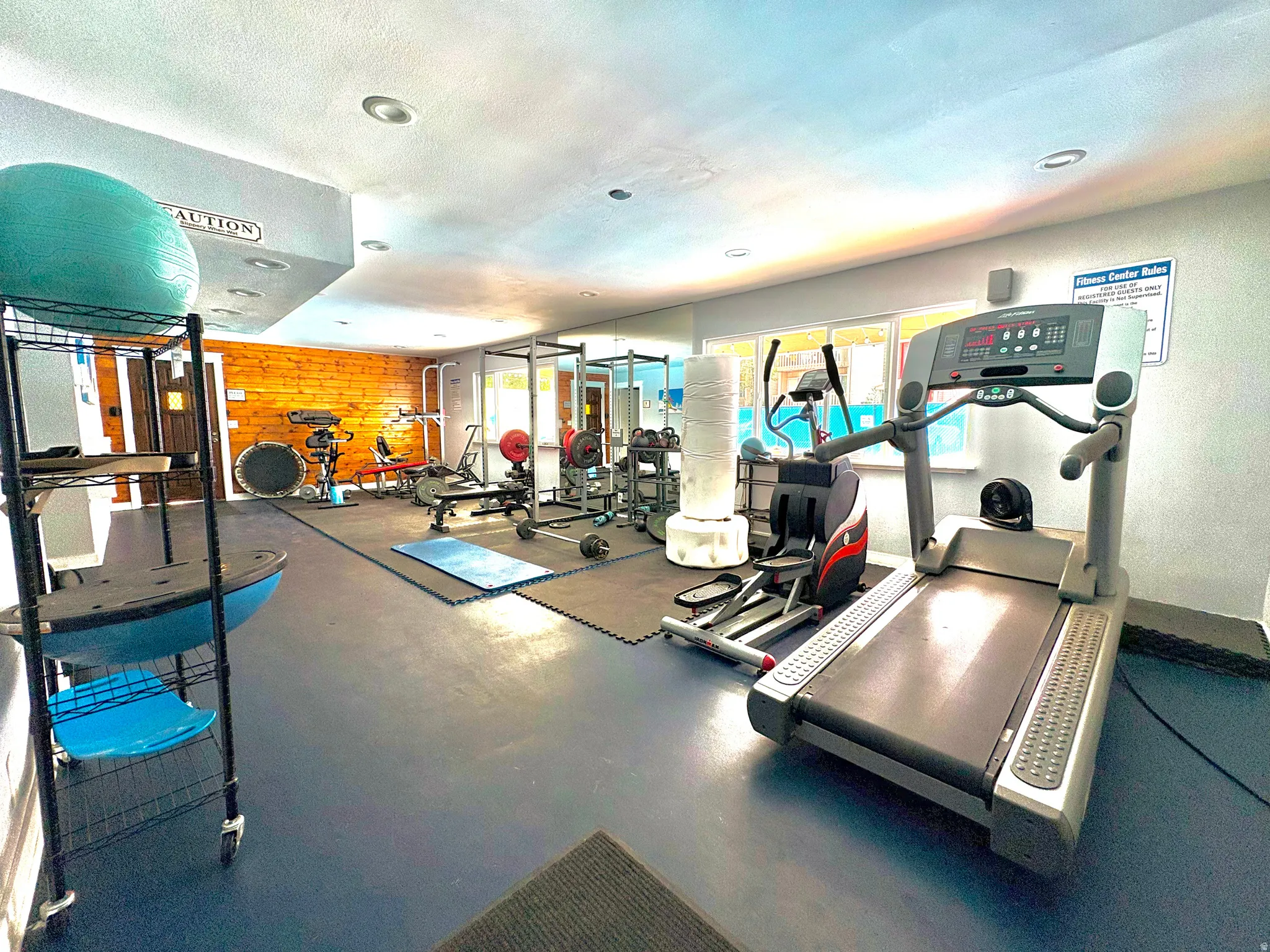 Dedicated fitness room featuring blue rubber flooring, recessed lighting, and a prominent wood-paneled accent wall