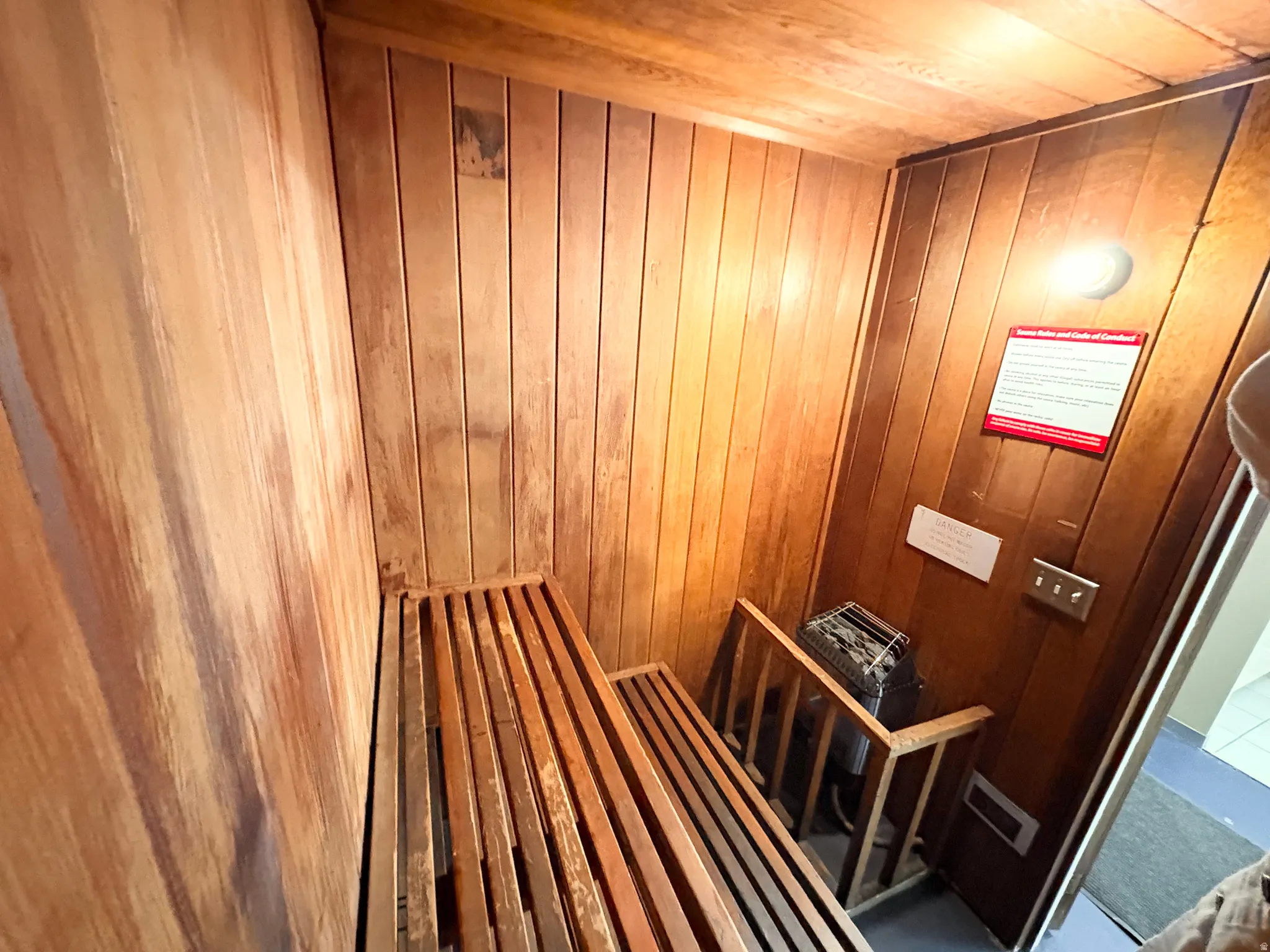 Dedicated sauna room featuring slatted wood benches, vertical wood paneling, and a built-in sauna heater unit