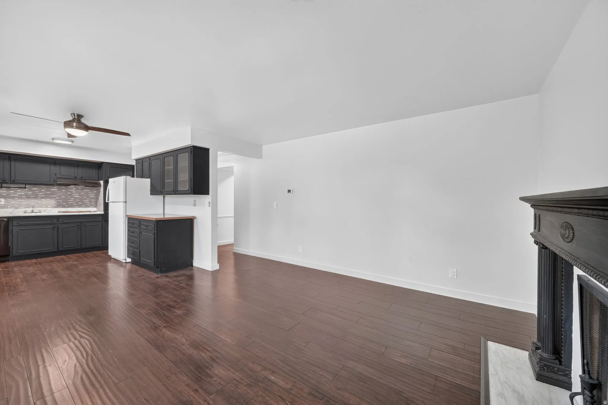 Open-concept living area featuring wood-finish flooring, a decorative fireplace with a dark wood mantel, and crisp white walls