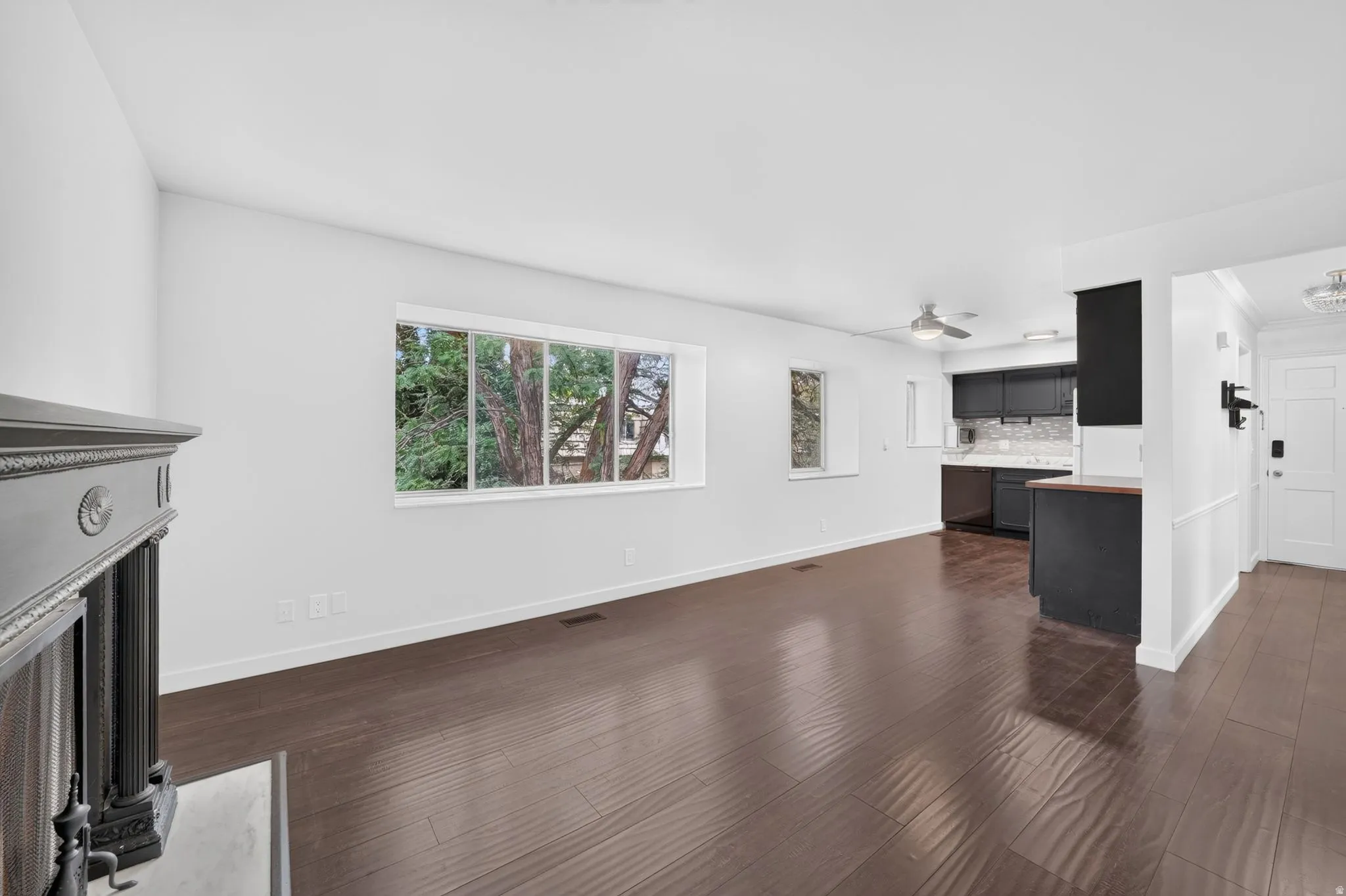 Open-concept living area featuring rich wood-finish flooring, a decorative fireplace mantel, and large windows