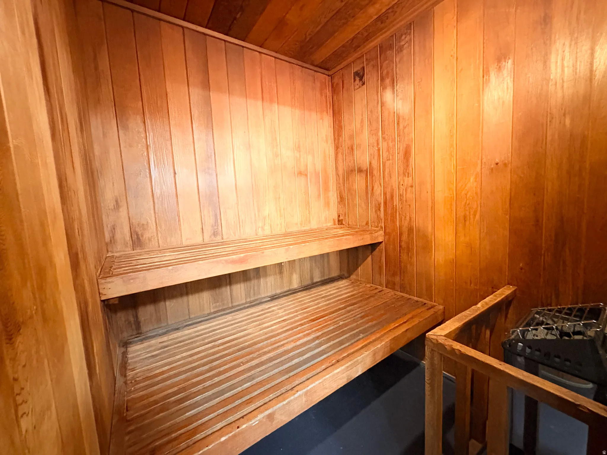 Dedicated sauna room featuring slatted wood paneling, multi-level slatted wooden benches, and a built-in sauna heater