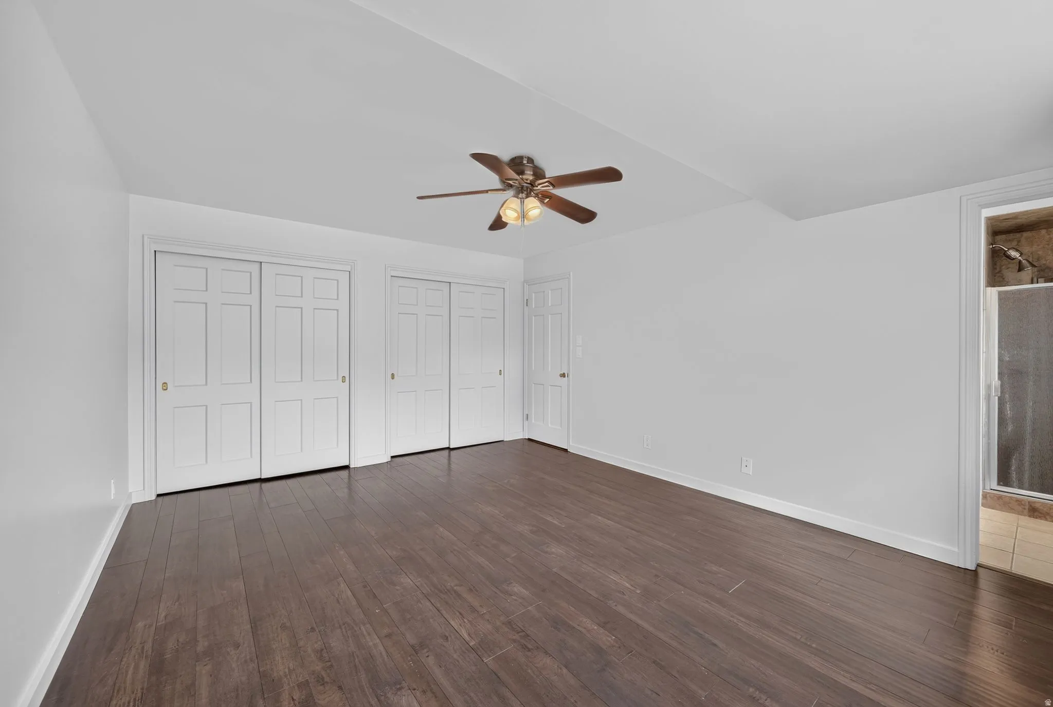 Spacious room featuring wood-finish flooring, white walls, and a ceiling fan with integrated lighting