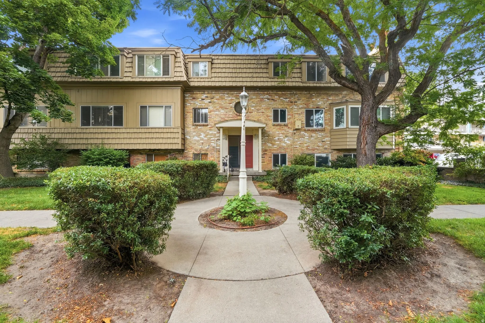 Multi-unit property with a brick and shingle facade, dormer windows, and mature trees