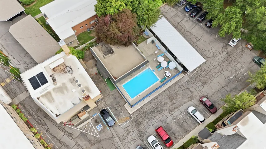 Outdoor swimming pool with surrounding patio space, shaded seating, and covered parking