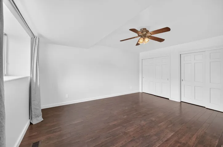 Spacious room featuring wood-finish flooring, white walls, and a ceiling fan with integrated lighting