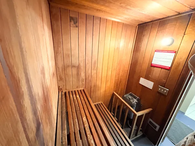 Dedicated sauna room featuring slatted wood benches, vertical wood paneling, and a built-in sauna heater unit