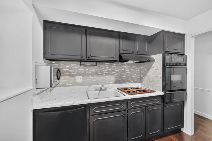 Kitchenette featuring dark cabinetry, white marble-finish countertop, and a mosaic tile backsplash