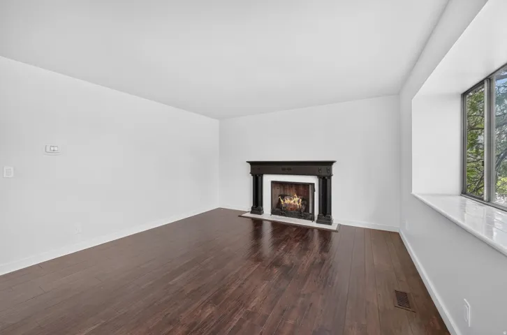 Bright living space featuring dark wood-finish flooring, a decorative fireplace with a dark wood mantel, and a large bay window with a white marble sill