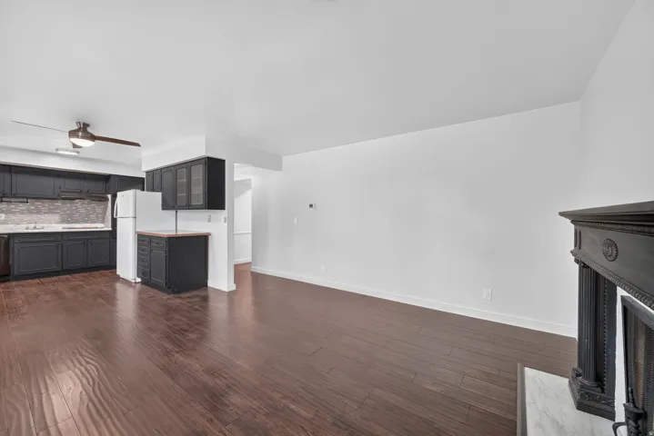 Open-concept living area featuring wood-finish flooring, a decorative fireplace with a dark wood mantel, and crisp white walls