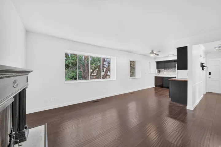 Open-concept living area featuring rich wood-finish flooring, a decorative fireplace mantel, and large windows