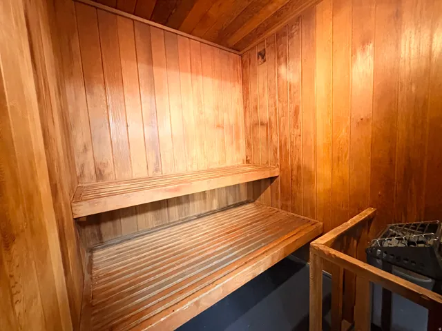Dedicated sauna room featuring slatted wood paneling, multi-level slatted wooden benches, and a built-in sauna heater