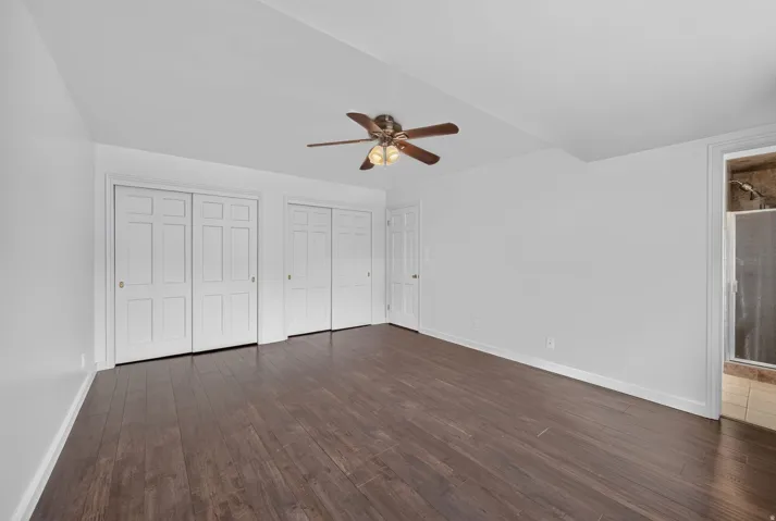 Spacious room featuring wood-finish flooring, white walls, and a ceiling fan with integrated lighting