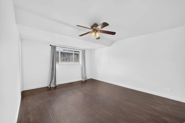 Spacious room featuring dark wood-finish flooring, white walls, and a window with natural light