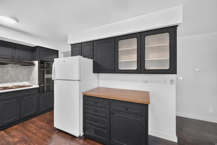 Kitchen featuring dark cabinetry, white countertops, built-in double ovens, and a tile backsplash