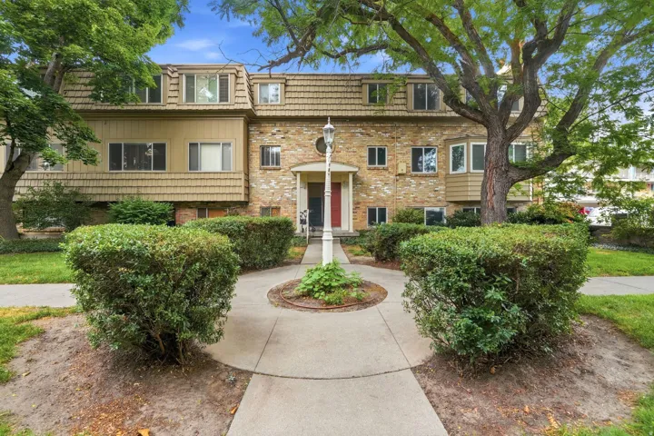 Multi-unit property with a brick and shingle facade, dormer windows, and mature trees