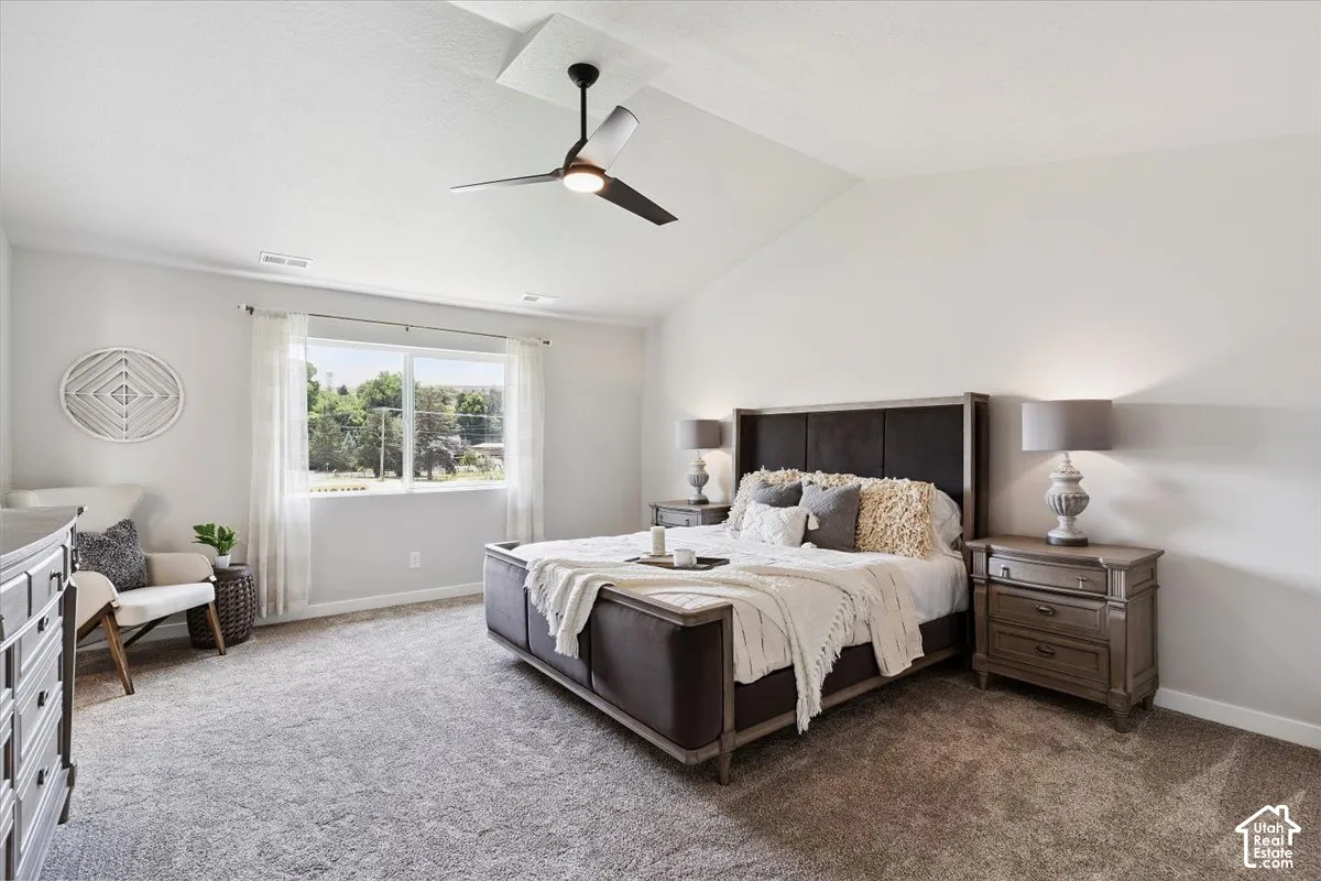 Spacious primary bedroom featuring vaulted ceilings, a large window, a ceiling fan with integrated lighting, two built-in nightstands, and soft carpeting