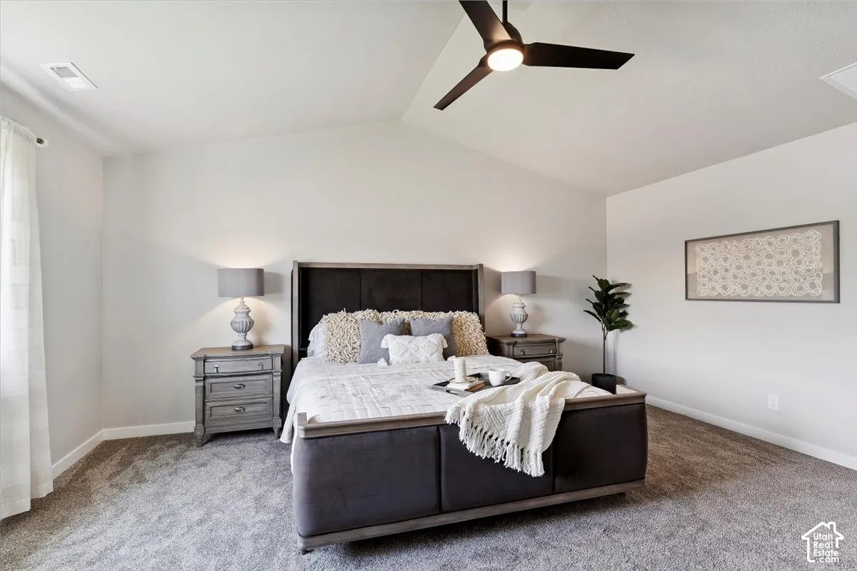 Primary bedroom featuring vaulted ceilings with light-toned walls, plush carpet flooring, a modern black ceiling fan, and white window sheers