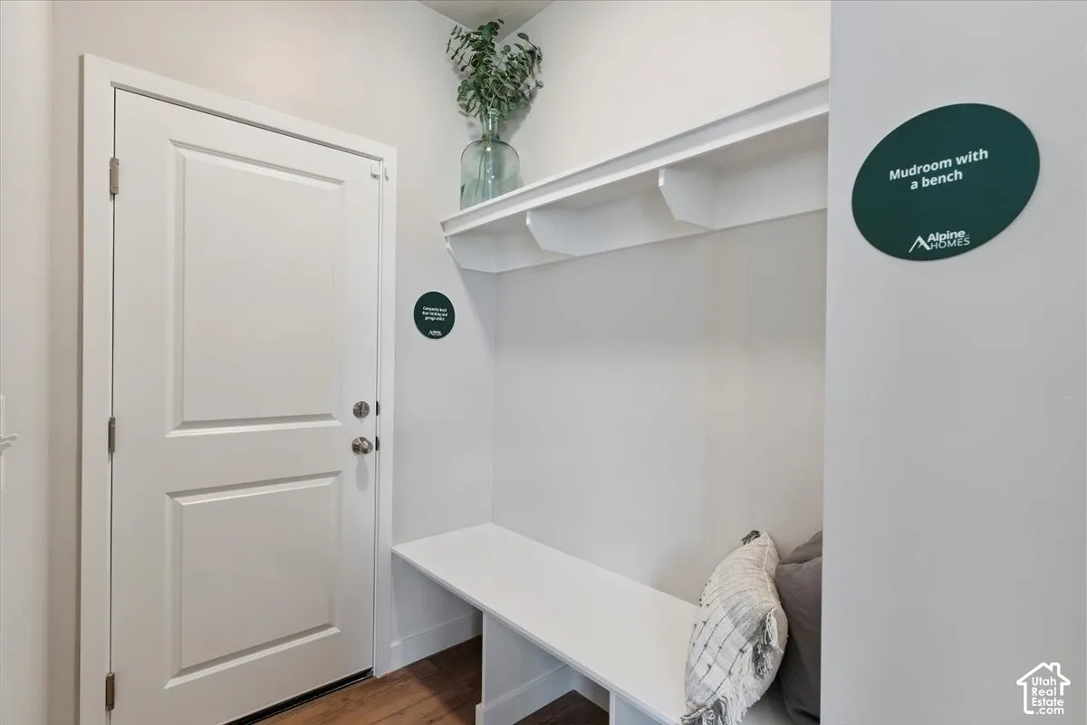 Garage entry & mudroom featuring a built-in bench, upper shelving, paneled door, and wood-finish flooring
