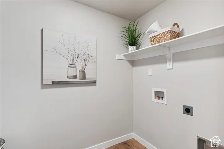Laundry room with light gray walls, wood-finish flooring, and white shelving