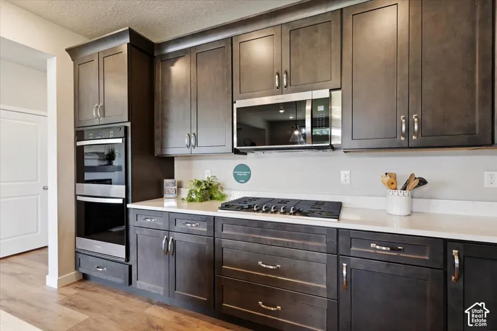 Gourmet kitchen featuring dark wood-finish cabinetry, stainless steel double wall ovens, a built-in microwave, a gas cooktop, and quartz countertops