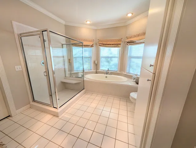 Bathroom featuring a corner soaking tub, a separate glass-enclosed shower with built-in bench, tiled flooring, crown molding, and recessed lighting