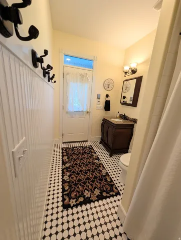 Bathroom featuring white beadboard paneling, black and white mosaic tile flooring, a wood vanity with a white sink, and a sconce light fixture