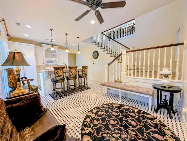 Open-concept living area featuring black and white mosaic tile flooring, a white kitchen with pendant lighting, and a detailed staircase with wood handrails