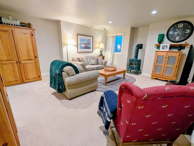 Recessed lighting illuminates this carpeted room featuring a window, built-in cabinetry, and a freestanding wood-burning stove