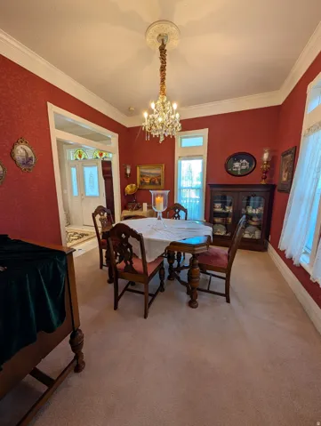 Formal dining space featuring patterned red walls, crown molding, a crystal chandelier with ceiling medallion, and light-colored carpeting