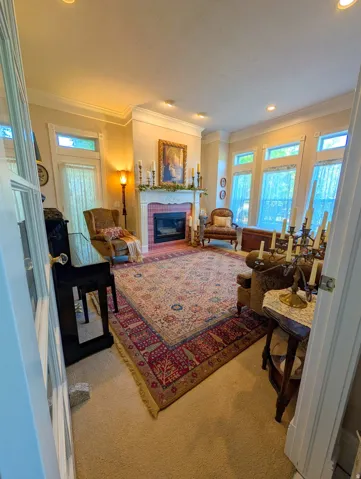 Living area featuring a central fireplace with decorative mantel, recessed lighting, crown molding, and multiple windows