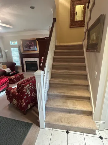 Carpeted staircase with white balusters and a dark wood handrail, featuring a prominent newel post