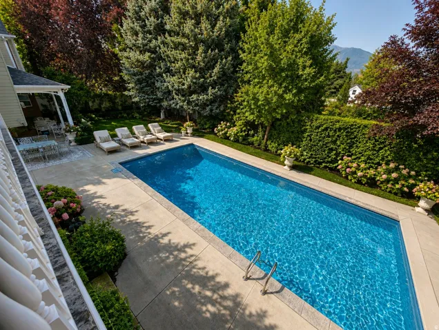 Rectangular swimming pool with integrated steps, surrounded by a concrete patio and mature landscaping