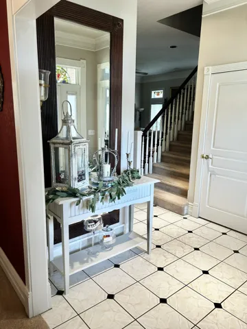 Foyer featuring patterned tile flooring with dark accent squares, a paneled entry door with fluted trim, and a staircase with white spindles and a dark handrail