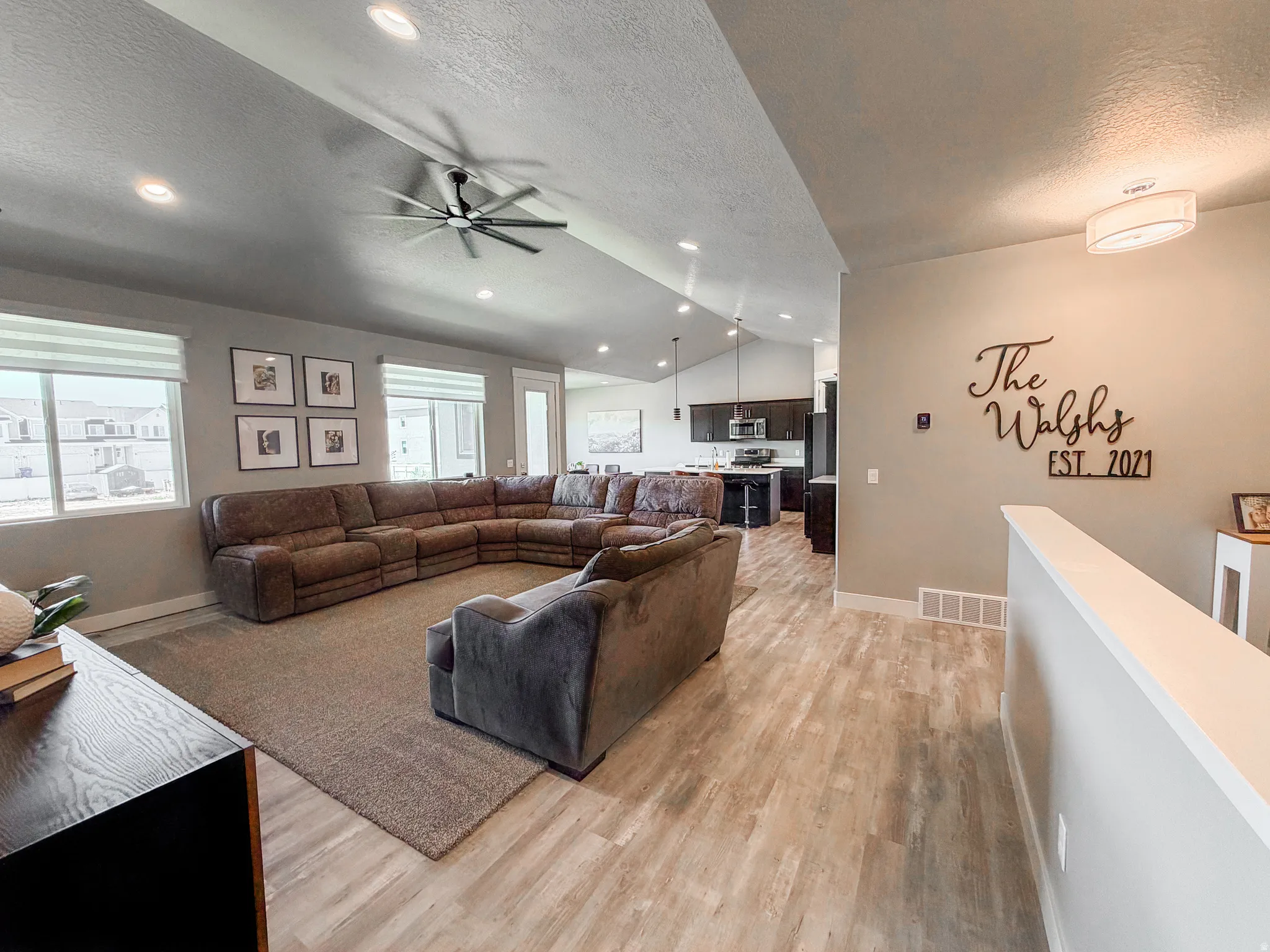 Spacious living area featuring wood-finish flooring, vaulted ceilings with recessed lighting, and a modern ceiling fan