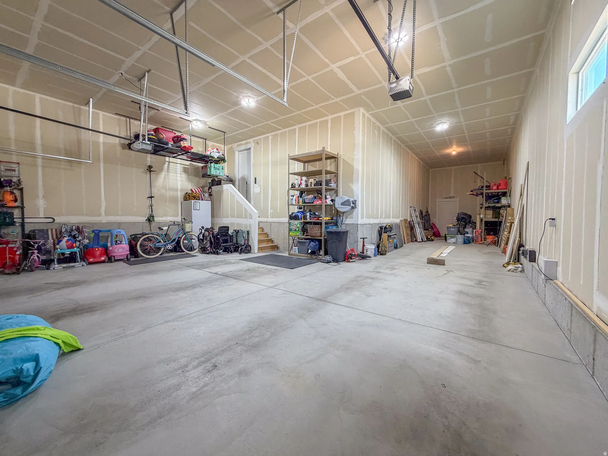 Spacious garage featuring a finished concrete floor, exposed ceiling joists, multiple recessed lighting fixtures, a side window, and a built-in staircase