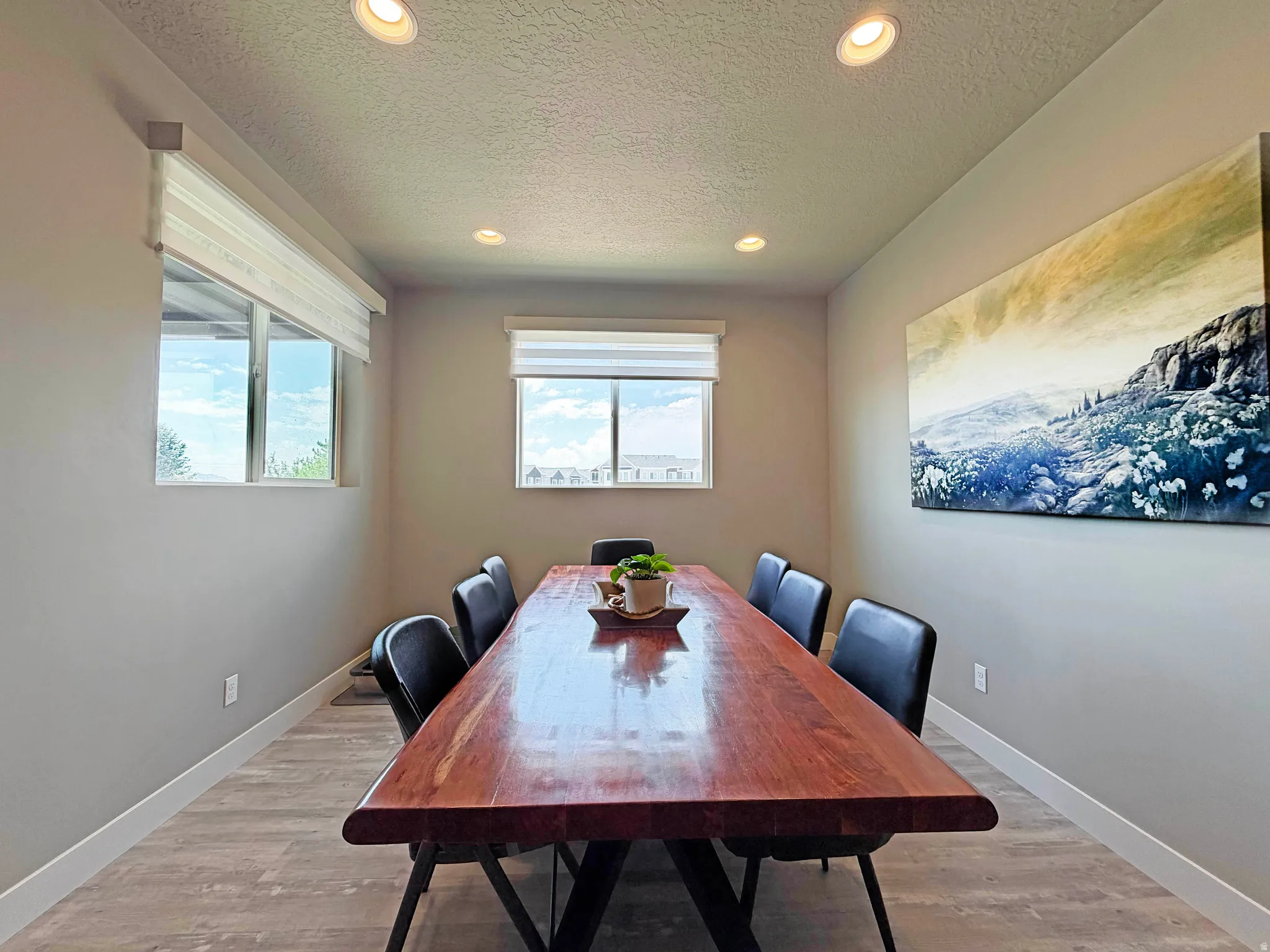 Dining area featuring a substantial wood-finish table, recessed ceiling lighting, two windows with roller shades, and wood-finish flooring