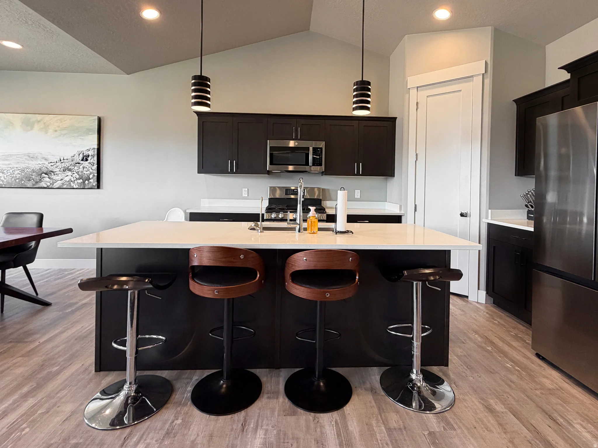 Modern kitchen with a spacious island featuring a light-toned countertop, dark cabinetry, stainless steel appliances, and wood-finish flooring
