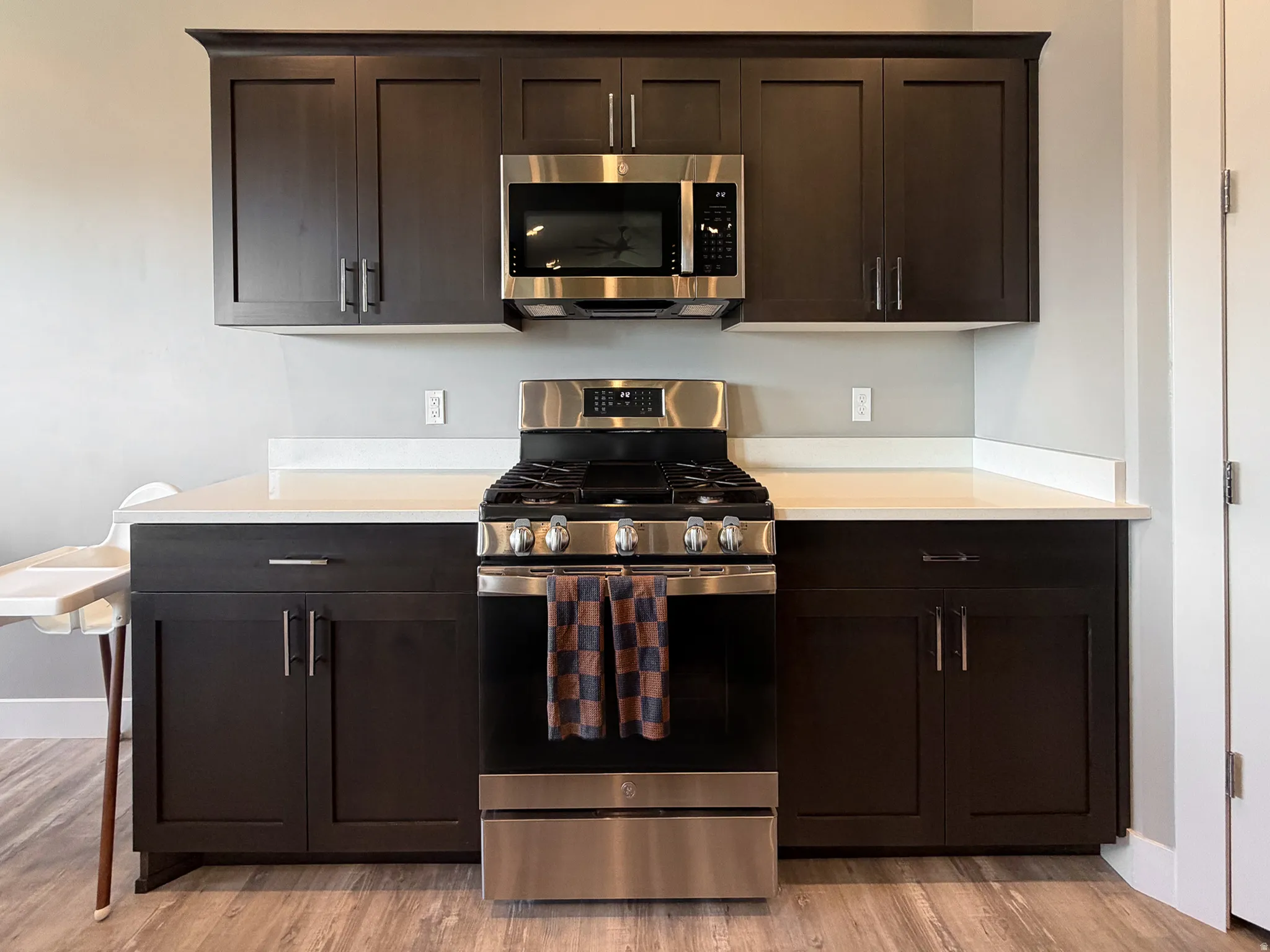 Kitchen featuring dark wood-finish cabinetry, stainless steel appliances, solid surface countertops, light gray walls, and wood-finish flooring