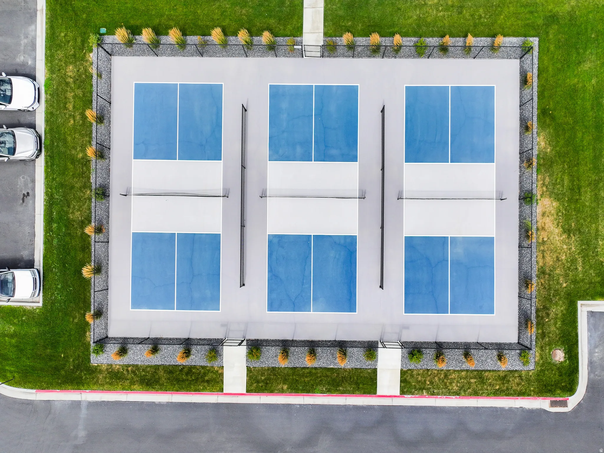 Three pickleball courts with blue and white playing surfaces, surrounded by a black chain-link fence