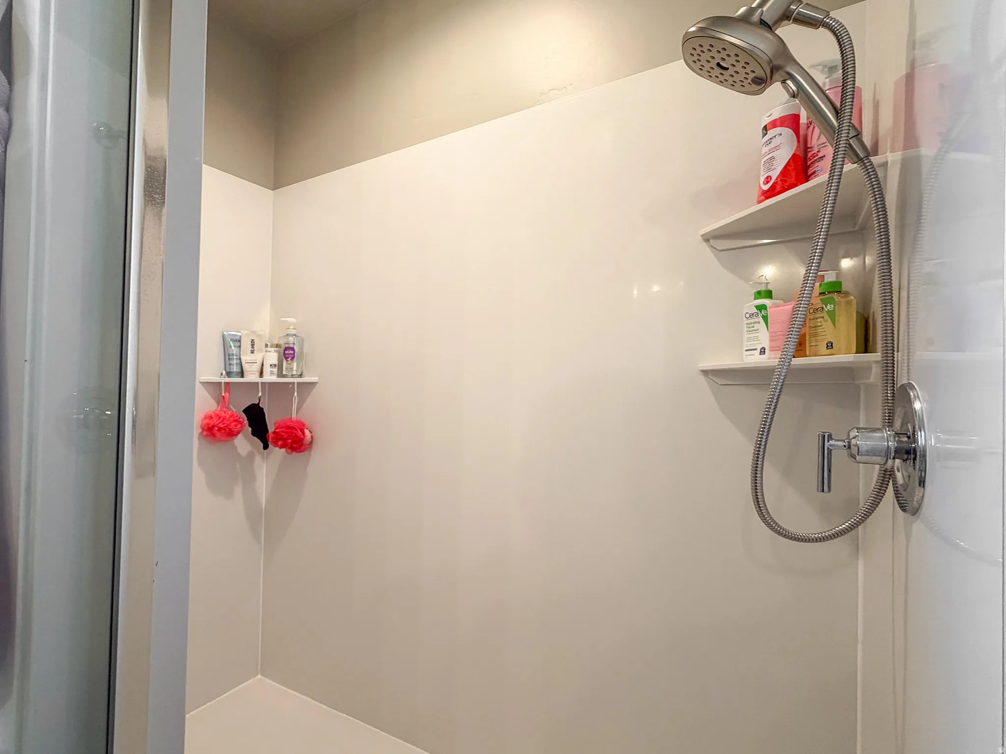 Shower stall featuring a handheld showerhead, chrome fixtures, built-in corner shelving, and a white finish