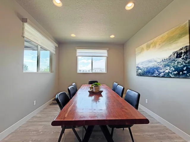 Dining area featuring a substantial wood-finish table, recessed ceiling lighting, two windows with roller shades, and wood-finish flooring