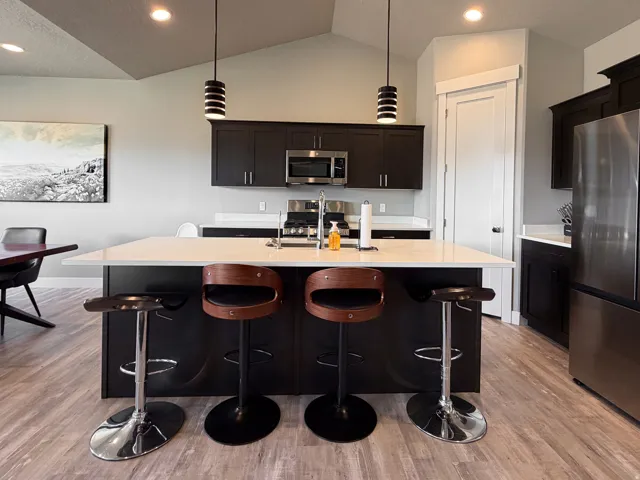 Modern kitchen with a spacious island featuring a light-toned countertop, dark cabinetry, stainless steel appliances, and wood-finish flooring