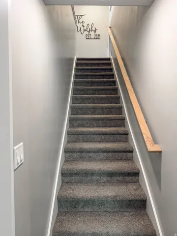Carpeted staircase with light gray walls and a wooden handrail