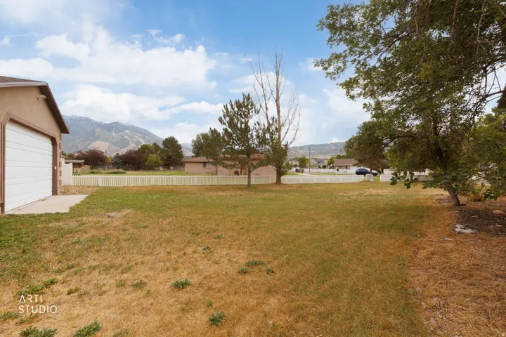Expansive yard space featuring a detached garage, white picket fencing, and mature trees