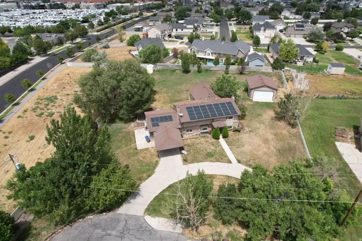 Residential property featuring a detached garage, solar panel array, mature trees, and a concrete driveway