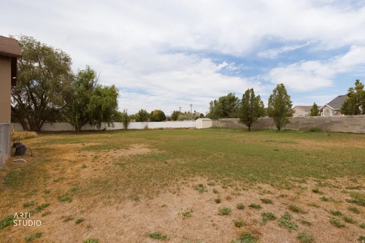 Expansive backyard featuring a large grass area, mature trees, a white perimeter fence, and a storage shed