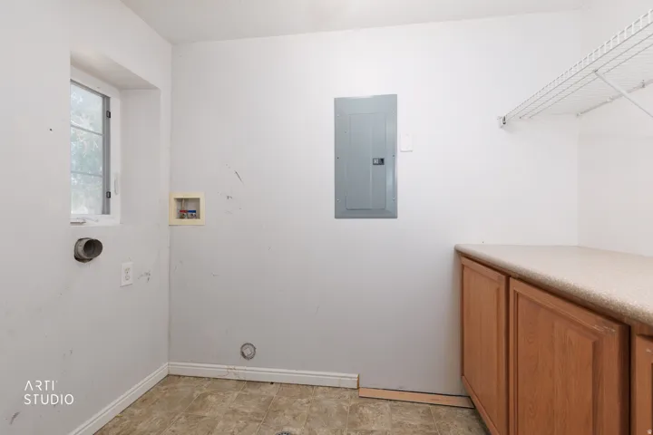 Laundry room featuring a window, wood-finish cabinetry, a light-toned countertop, and wire shelving