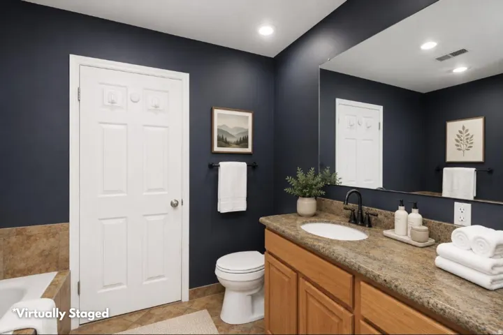 Bathroom featuring a light wood-finish vanity with a granite-style countertop, a white oval undermount sink, and a matte black single-handle faucet