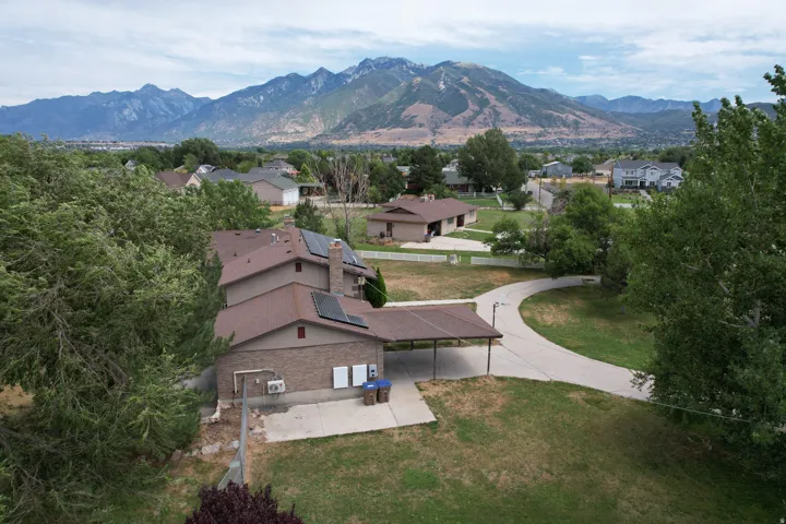 Mountainous backdrop framing a property with a long, paved driveway, a carport, and multiple solar panels visible on the roof